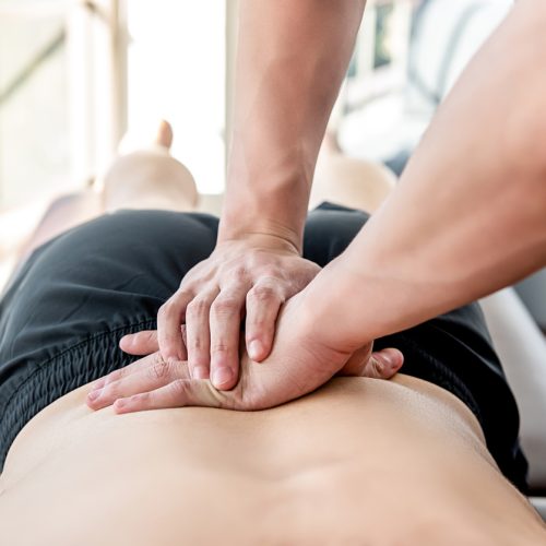 Therapist giving lower back sports massage to athlete male patient in clinic